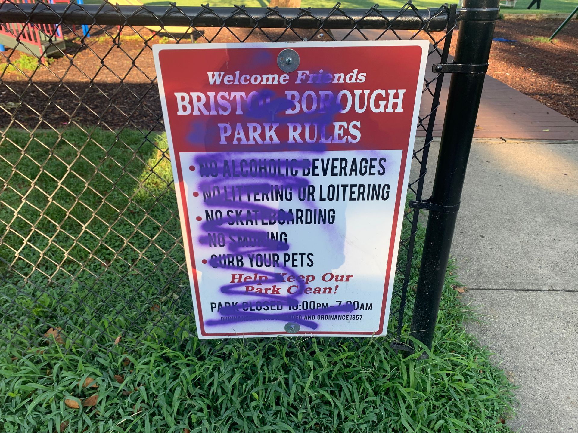 Sign with park rules in Bristol Borough, partially obscured by purple graffiti.