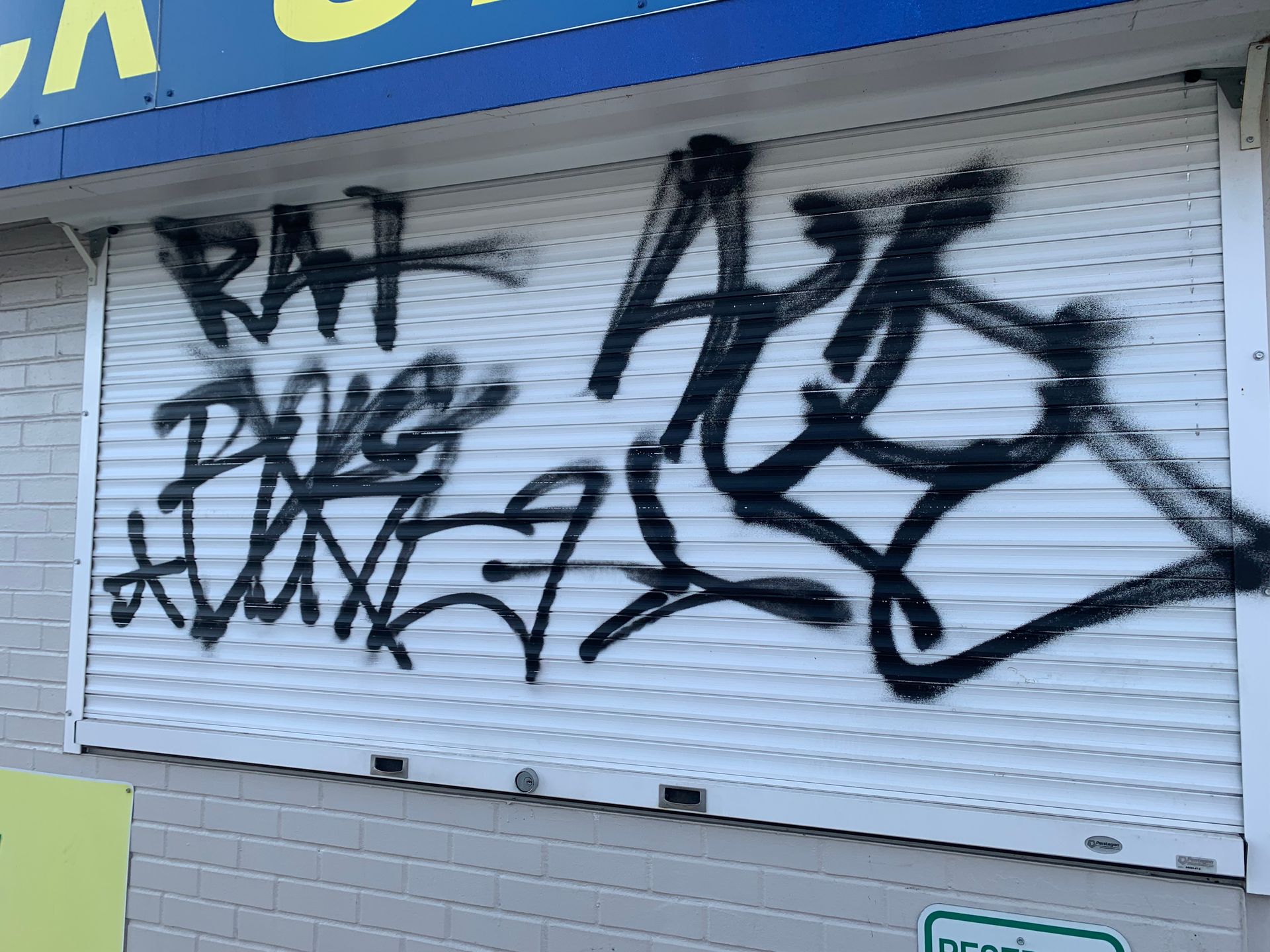 Graffiti on a white store security shutter. Black spray-painted words: 