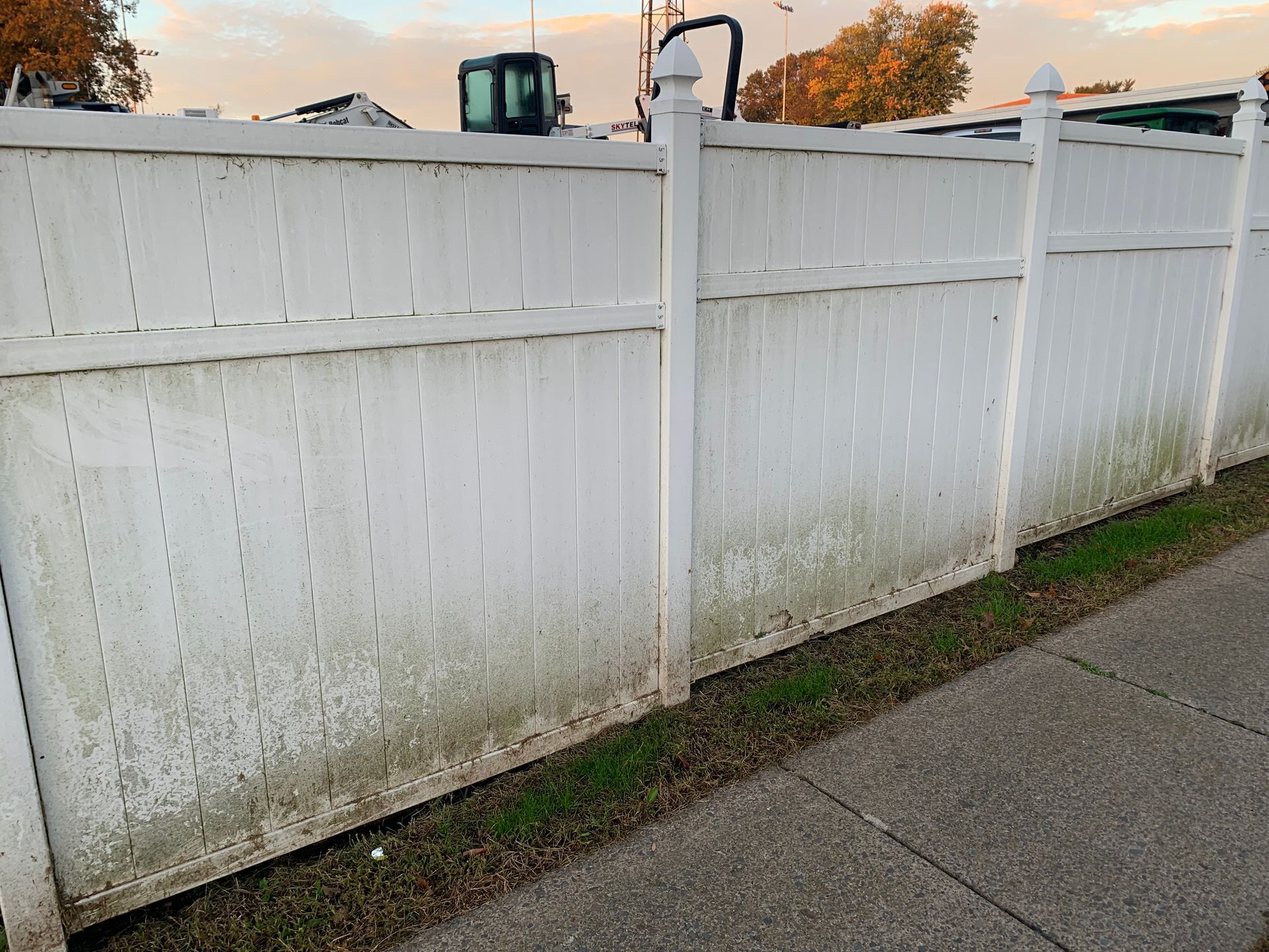 White vinyl fence with algae, alongside a sidewalk and grass.