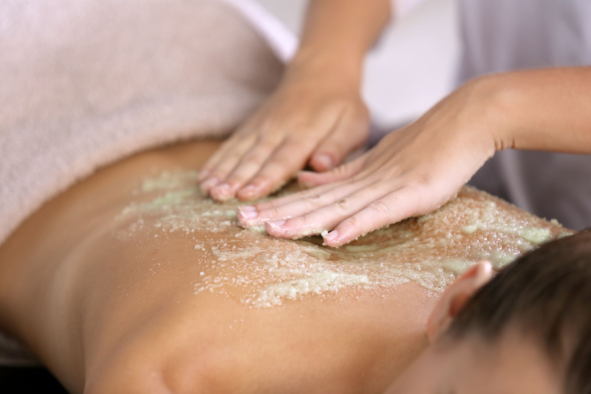 Hands exfoliating a person’s back with scrub in a spa setting
