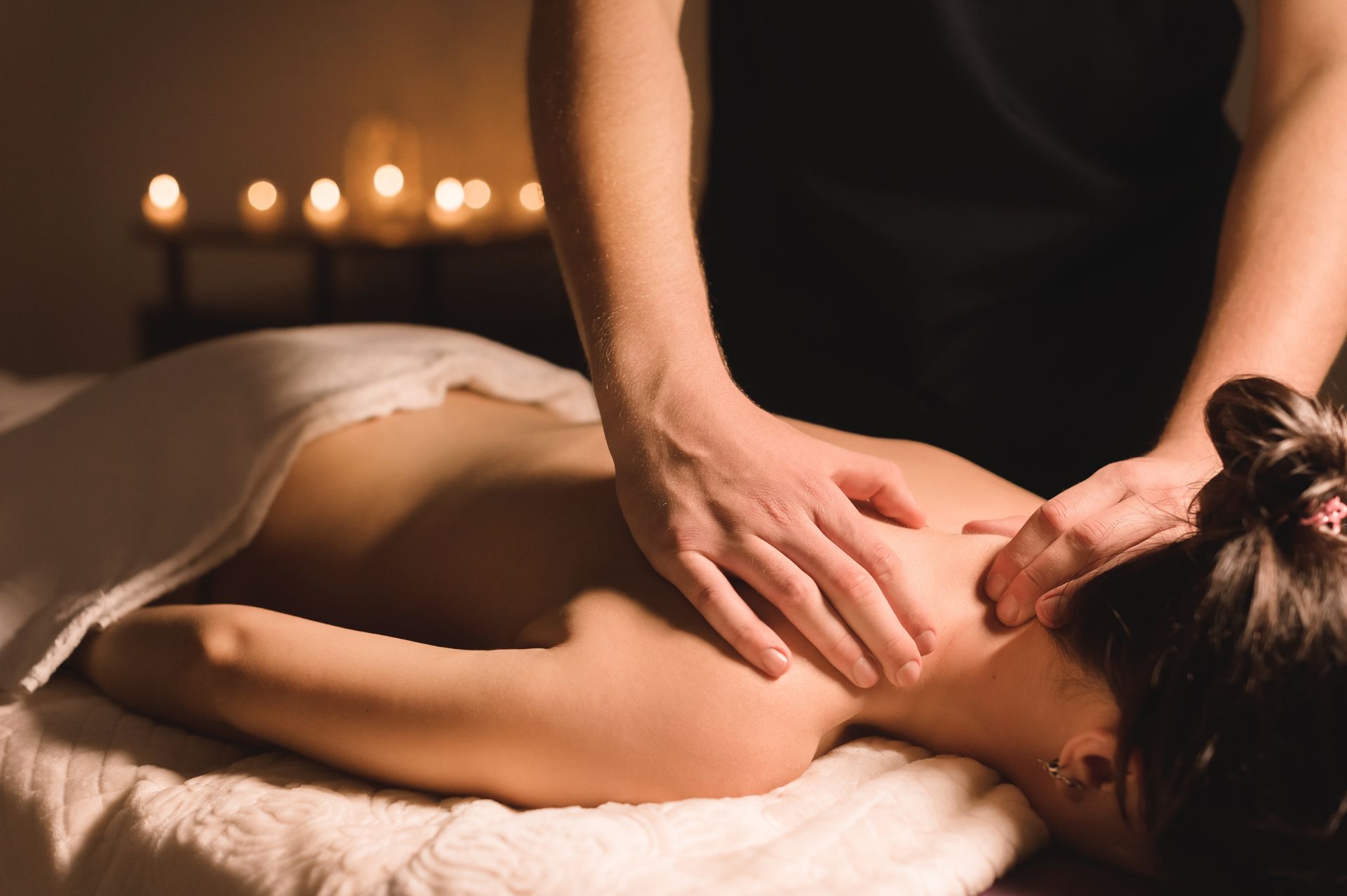 Spa massage therapist giving a back massage with candles in the background