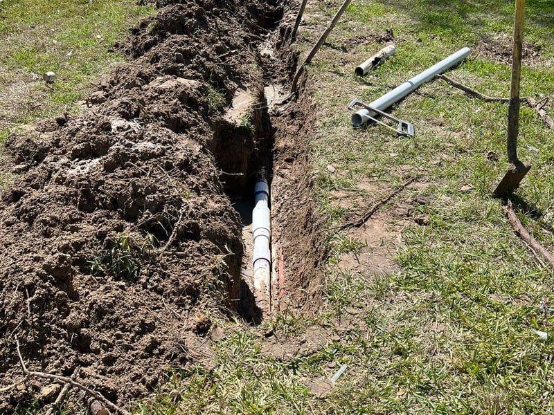 Trenched utility pipe with exposed white and blue sections in a dirt excavation outdoors
