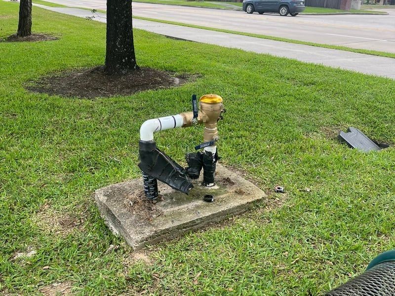 Outdoor water meter and pipe assembly on a concrete pad in a grassy roadside area.
