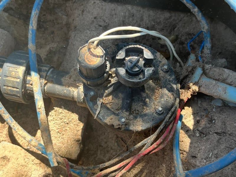 Close-up of a dirty pump or valve assembly with wires and pipes in a dusty outdoor setting
