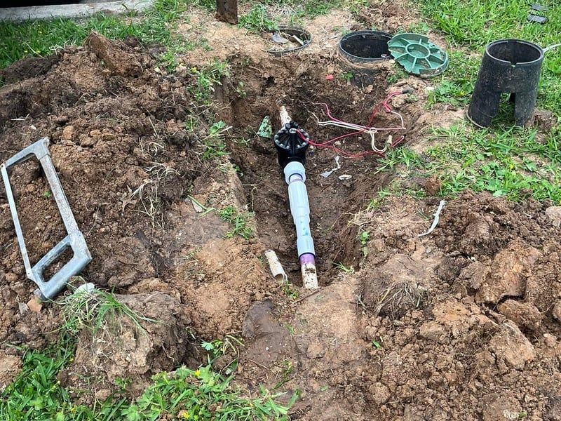 Underground pipe repair in a muddy trench with tools and exposed fittings.