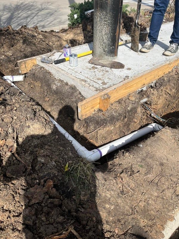 Concrete footing with metal post, wooden formwork, and PVC pipe trench at a construction site