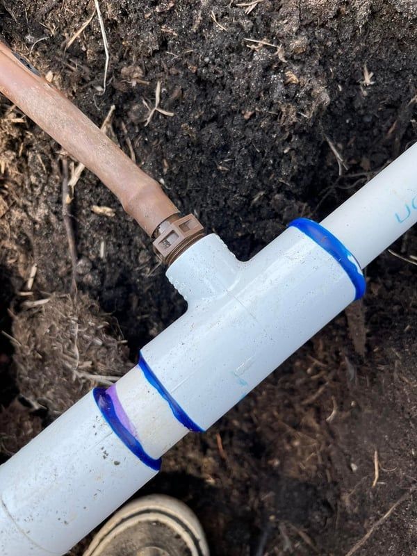 White PVC pipe with blue bands connected to a copper pipe in muddy soil outdoors