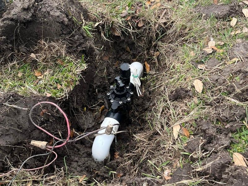 White pipe and black hoses in a muddy trench with a red cable on the ground