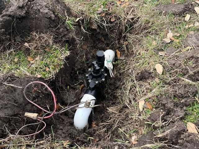 White pipe and black cables in a muddy trench with grass and leaves around it