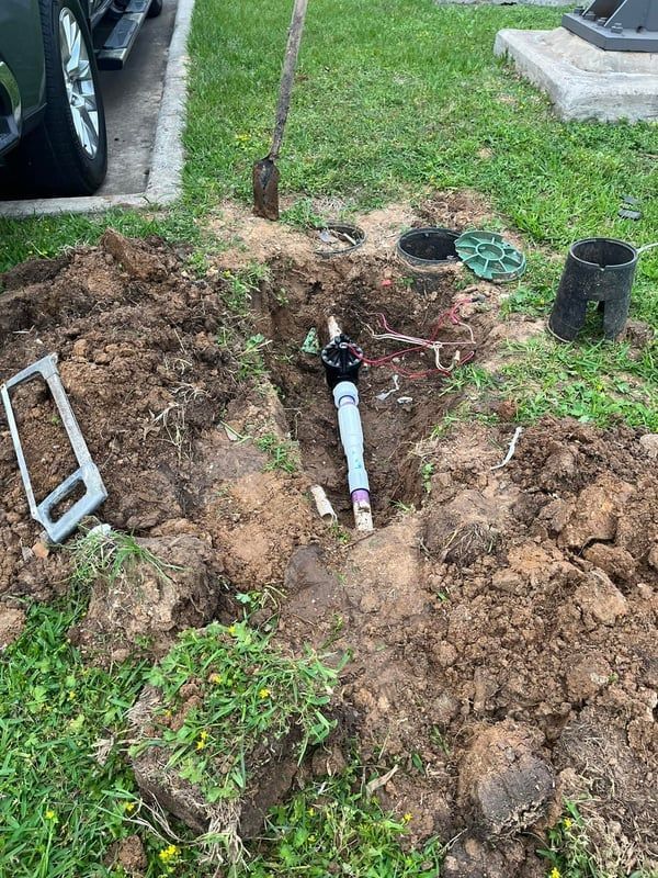 Small yard excavation exposing a white pipe and black fittings near a house lawn