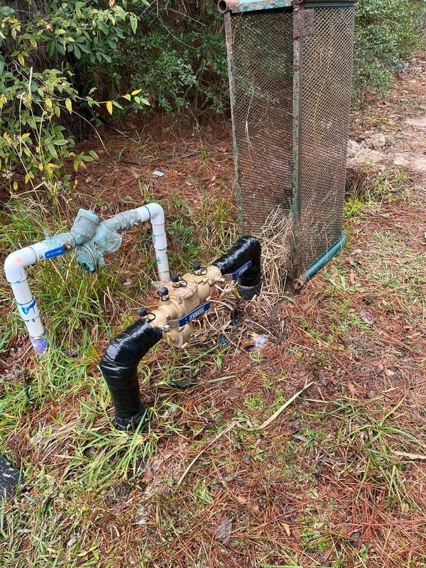 Outdoor water pipes and valves beside a wire fence on muddy ground