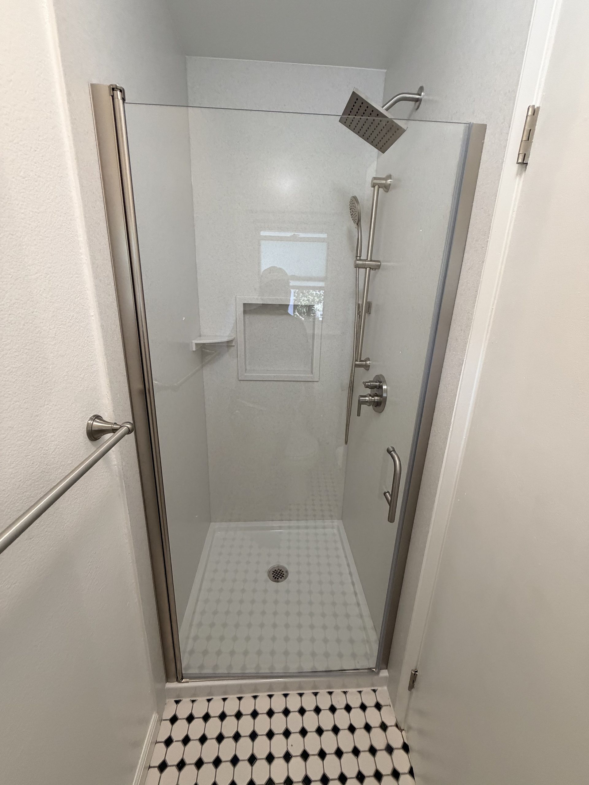Narrow bathroom shower stall with white tiles, glass door, and ceiling showerhead.