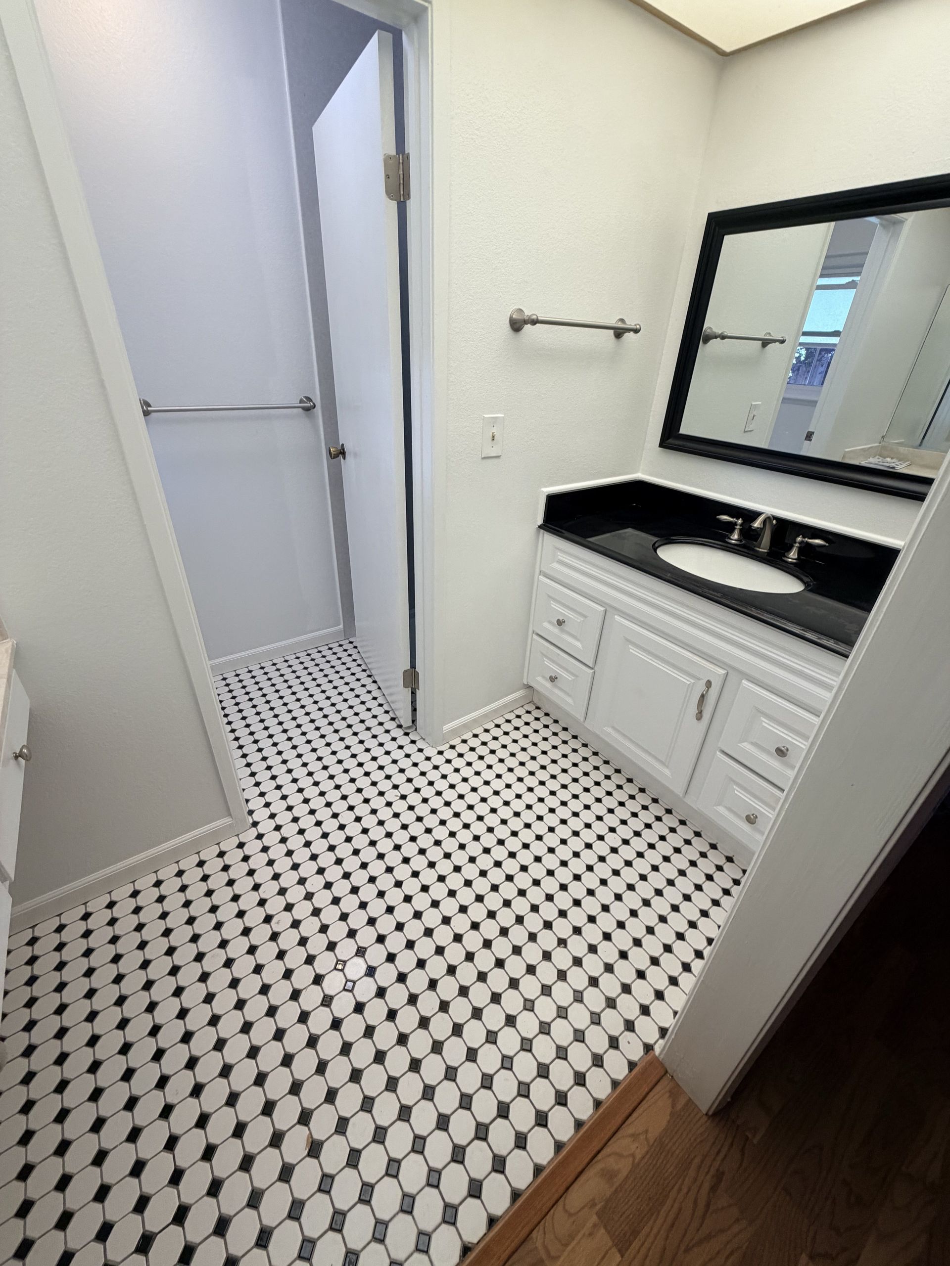 Small bathroom with black-and-white tile floor, white vanity, mirror, and open door to hallway