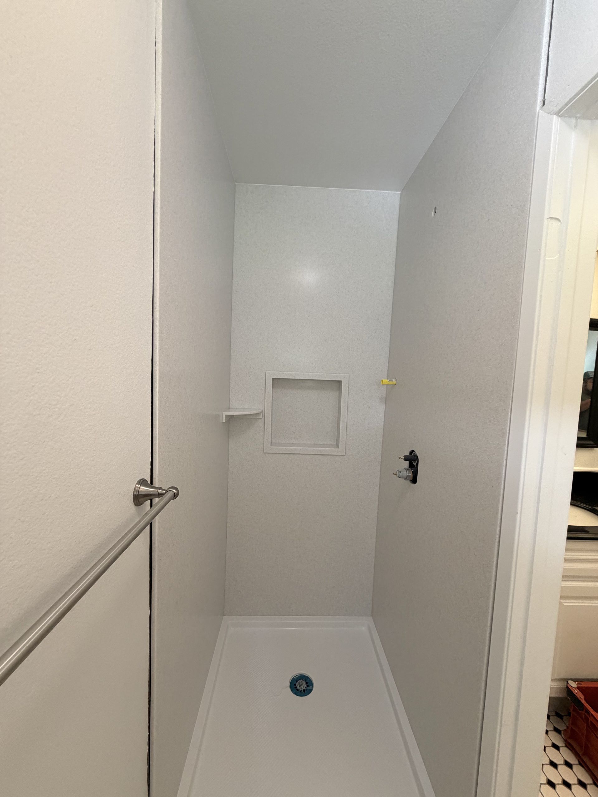 Empty white shower stall with built-in niche and drain, viewed from the doorway