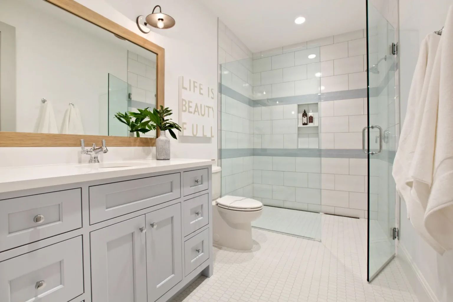 Bathroom with white and blue tile, glass shower, light blue vanity, and a large mirror.