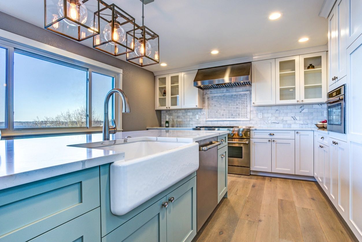 Modern kitchen with white cabinets, blue island, stainless steel appliances, and large window.