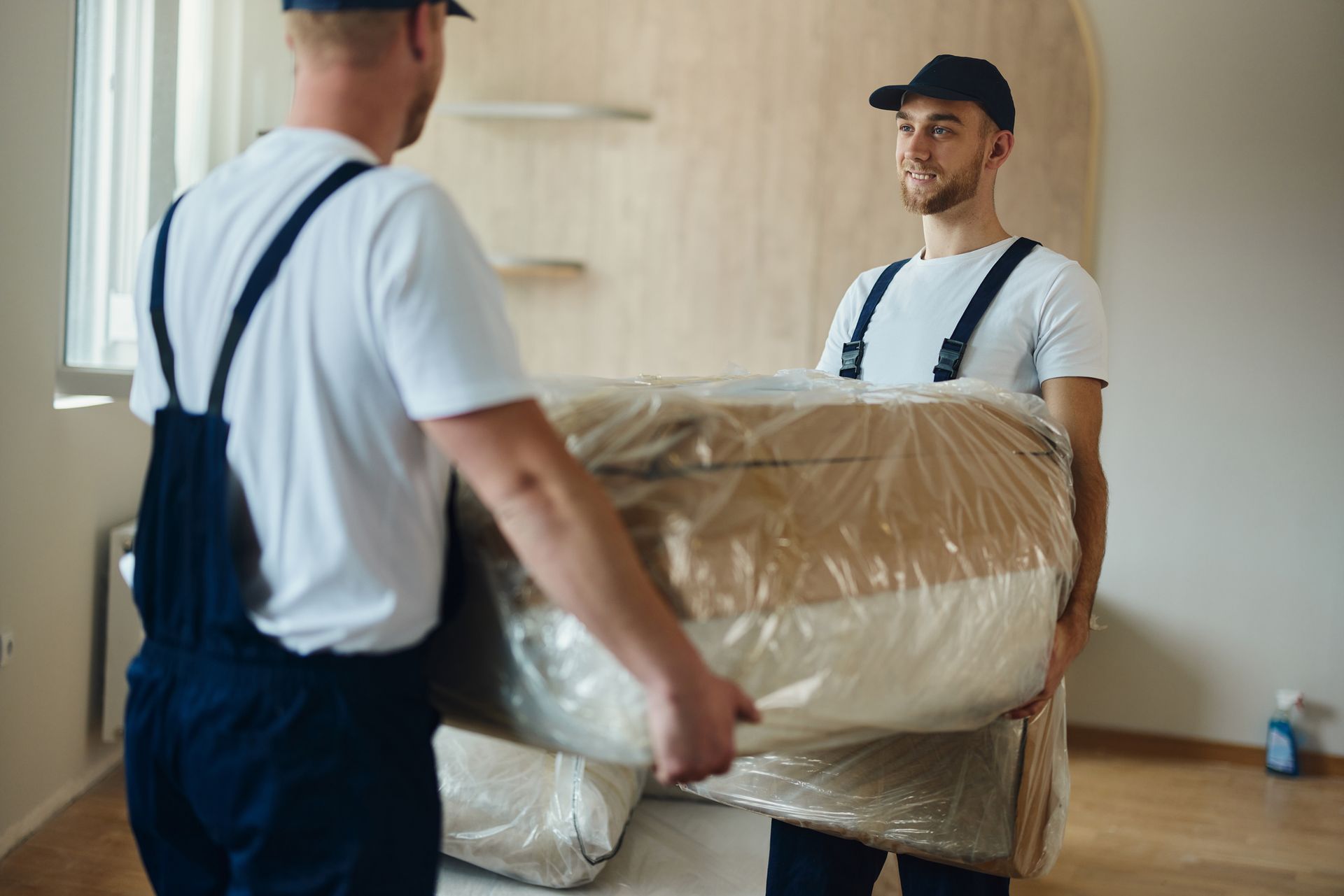 Two men are carrying a mattress in a plastic bag.