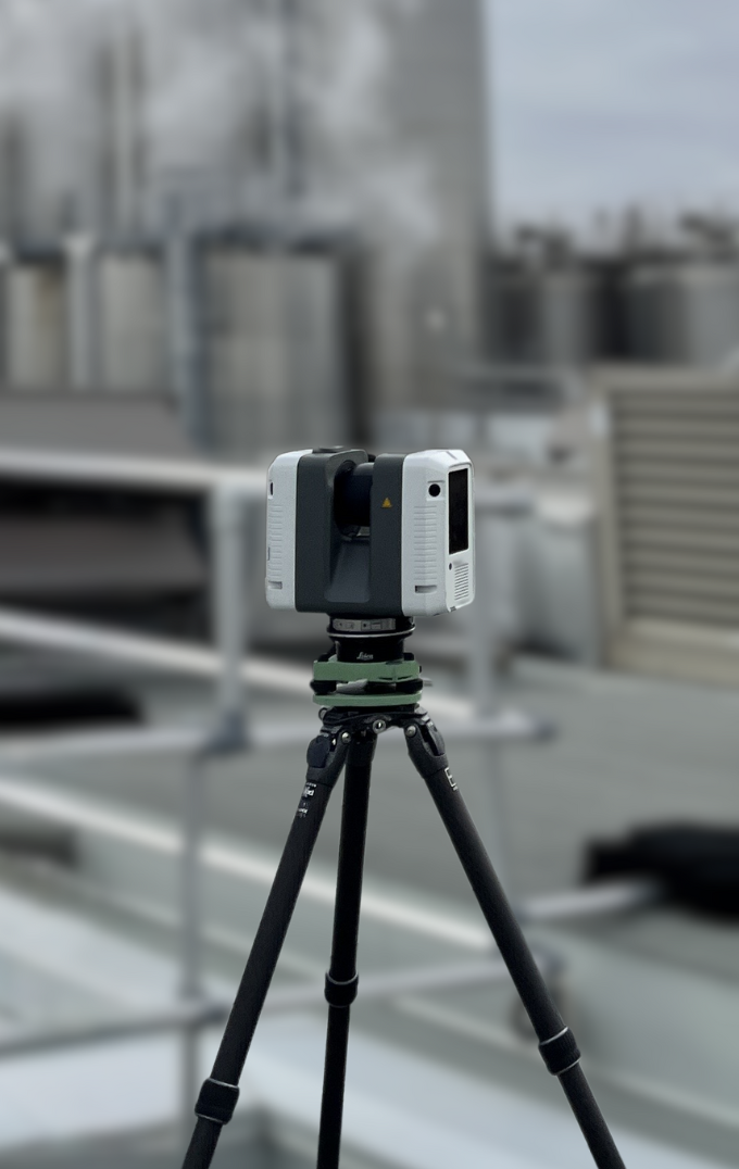 White and gray 3D scanner on tripod, scanning an industrial roof with tanks and steam.
