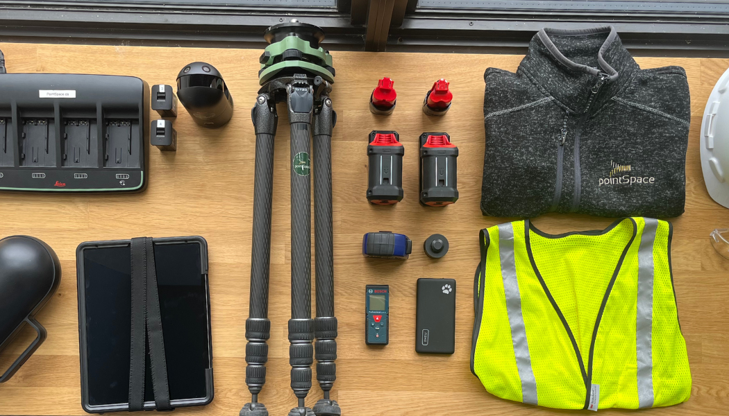 Equipment laid out on a table: tripod, charger, batteries, vest, tablet, and other surveying tools.