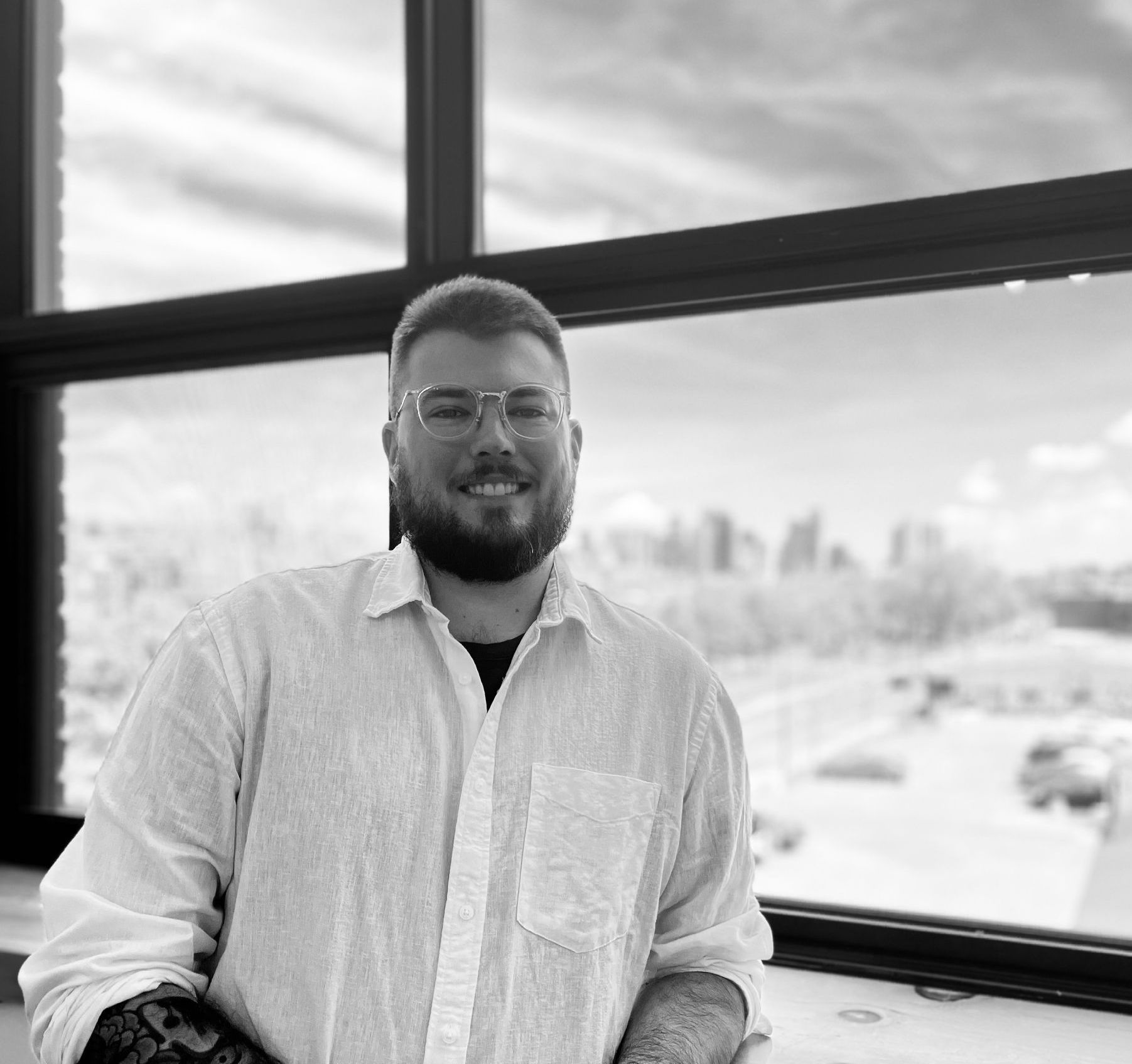 Smiling man in a white shirt standing by a large window overlooking a snowy city.