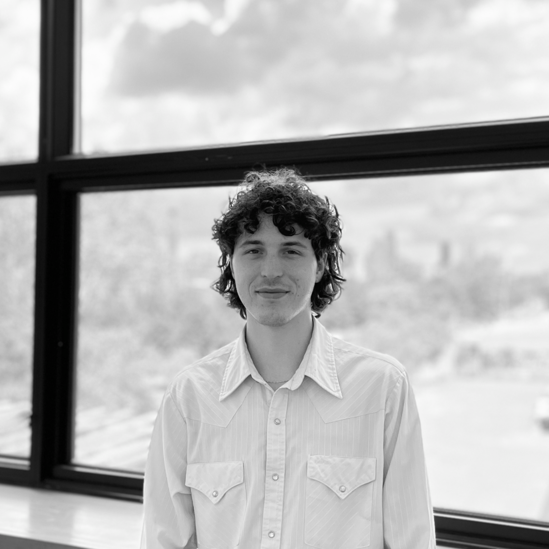 Portrait of a person in a white shirt standing by a large window in black and white