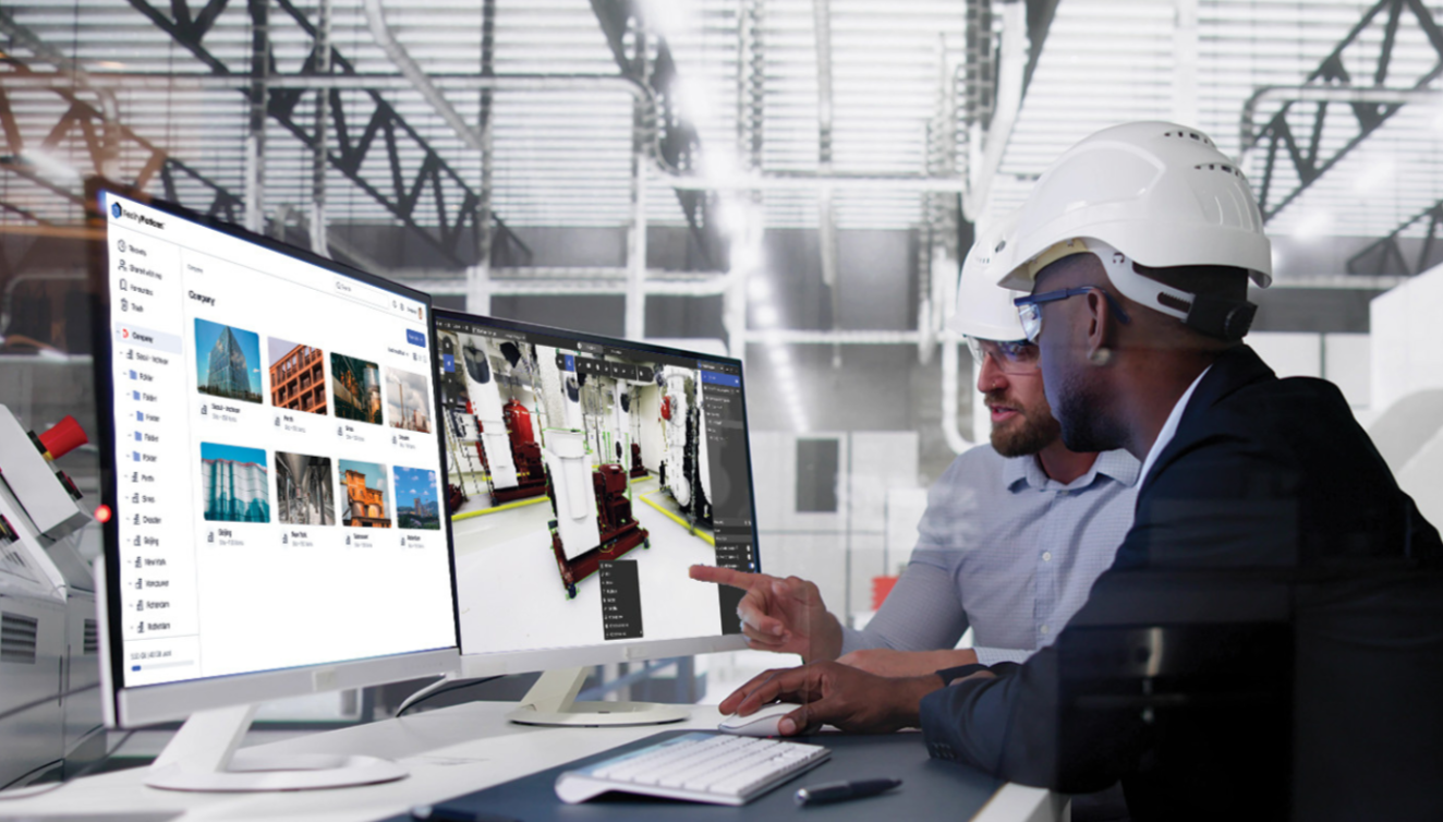 Two engineers in hard hats review a computer monitor in a bright industrial workspace.