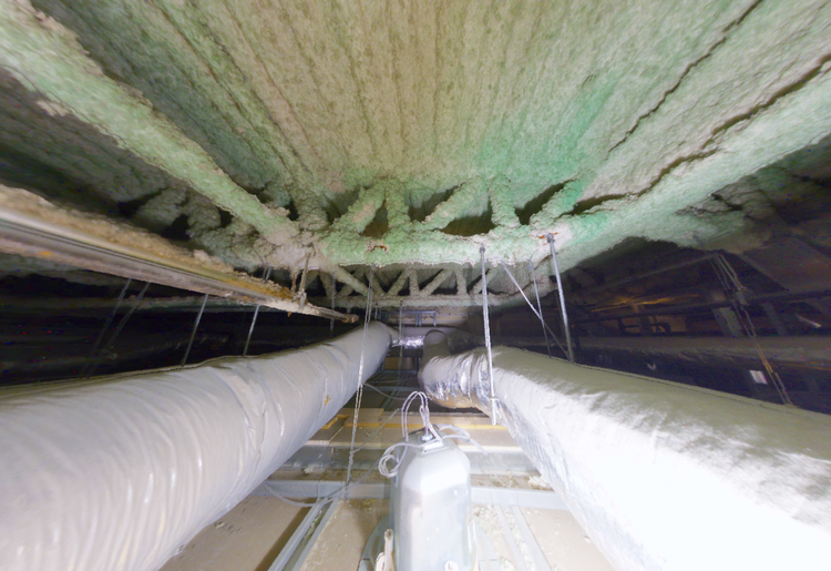 View from below of ceiling with pipes and insulation. Greenish-beige insulation covers beams; silver pipes run parallel.