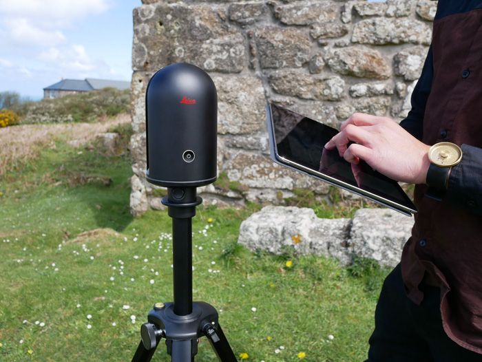 Person using a tablet beside a black post-mounted camera outdoors near a stone wall