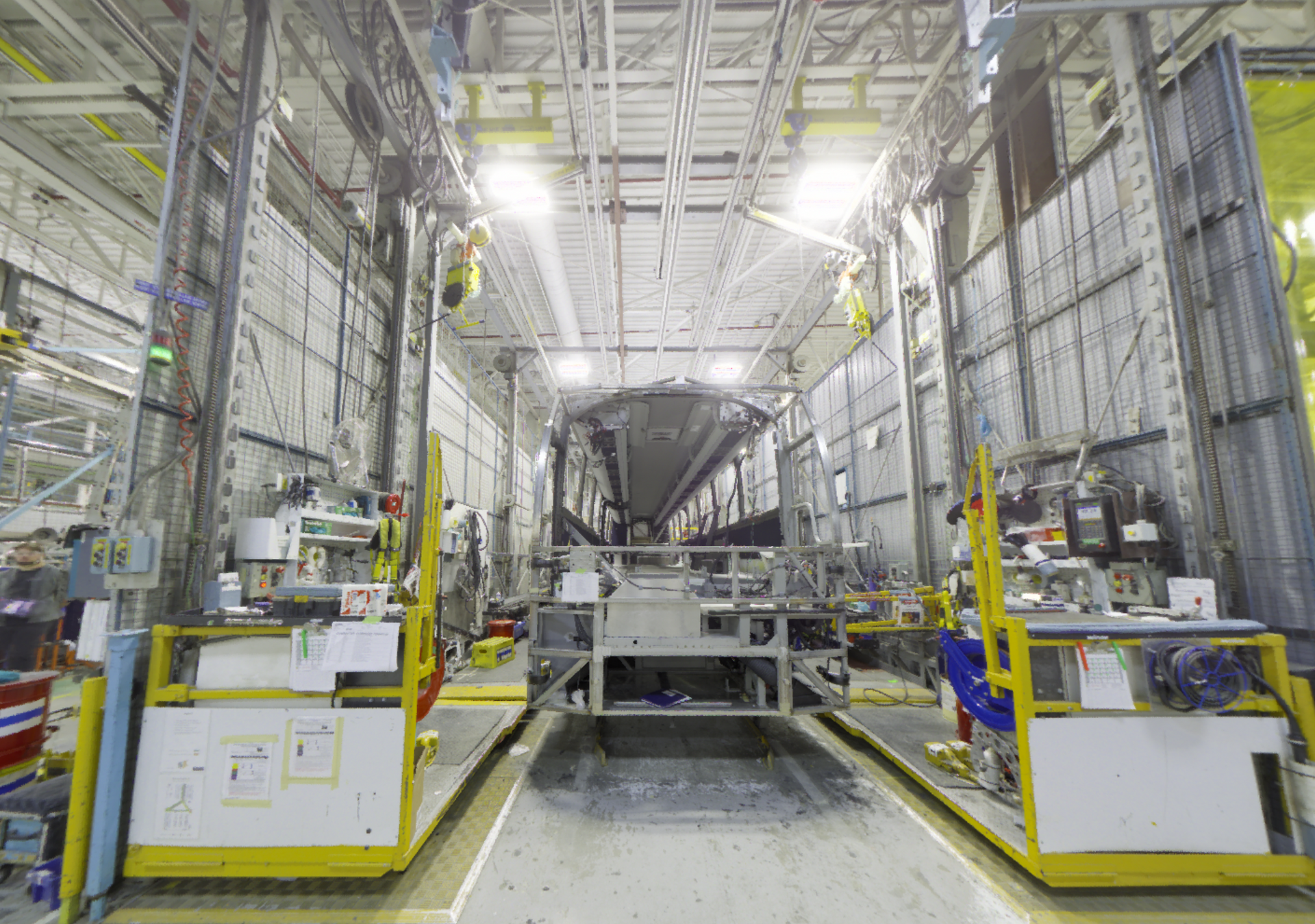 Intérieur d'une grande installation industrielle avec un étage de fusée ou de vaisseau spatial centré entre des plateformes de travail et des échafaudages.