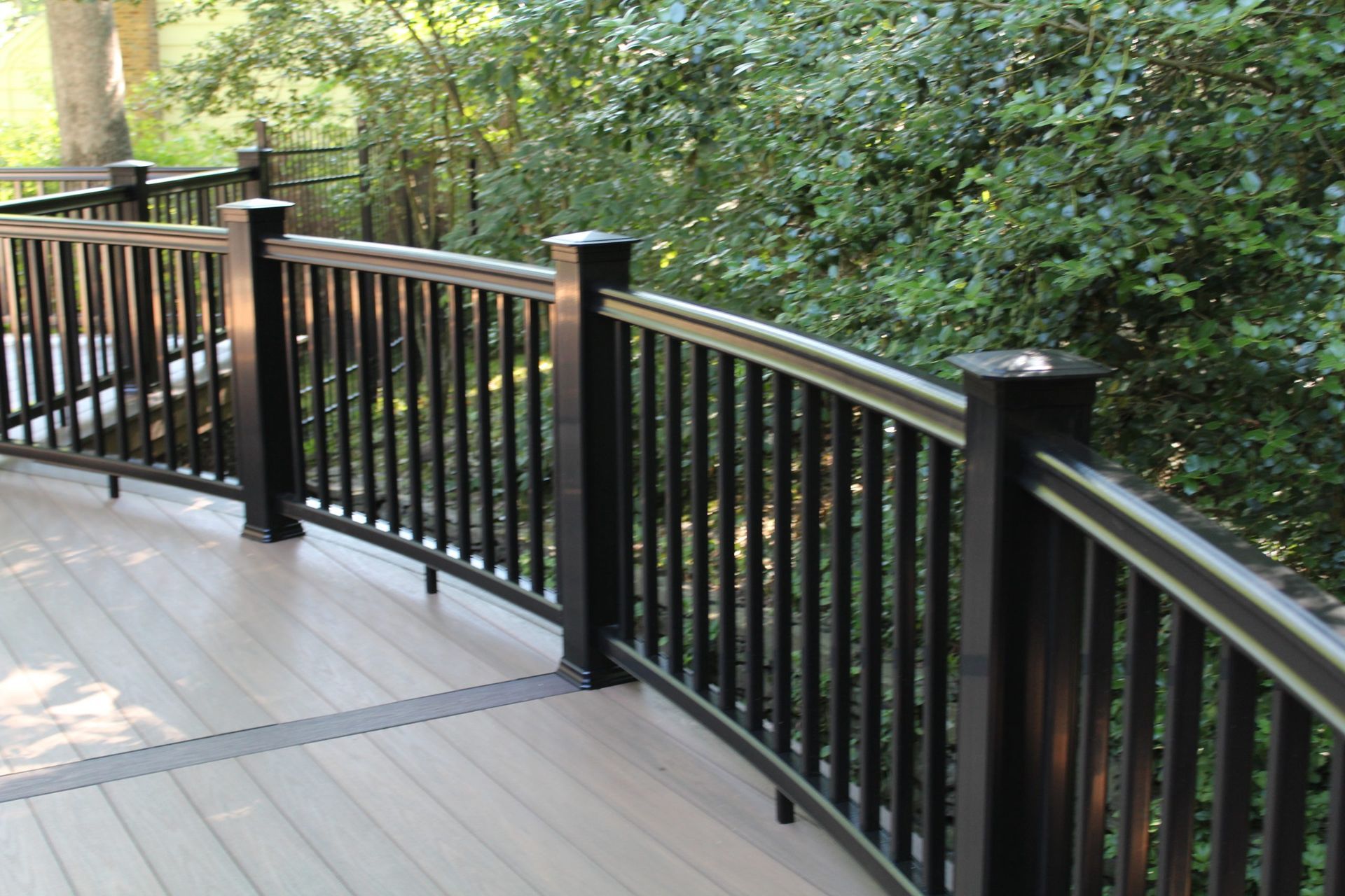 Curved composite deck railing installation surrounded by greenery by New Dimensions NJ