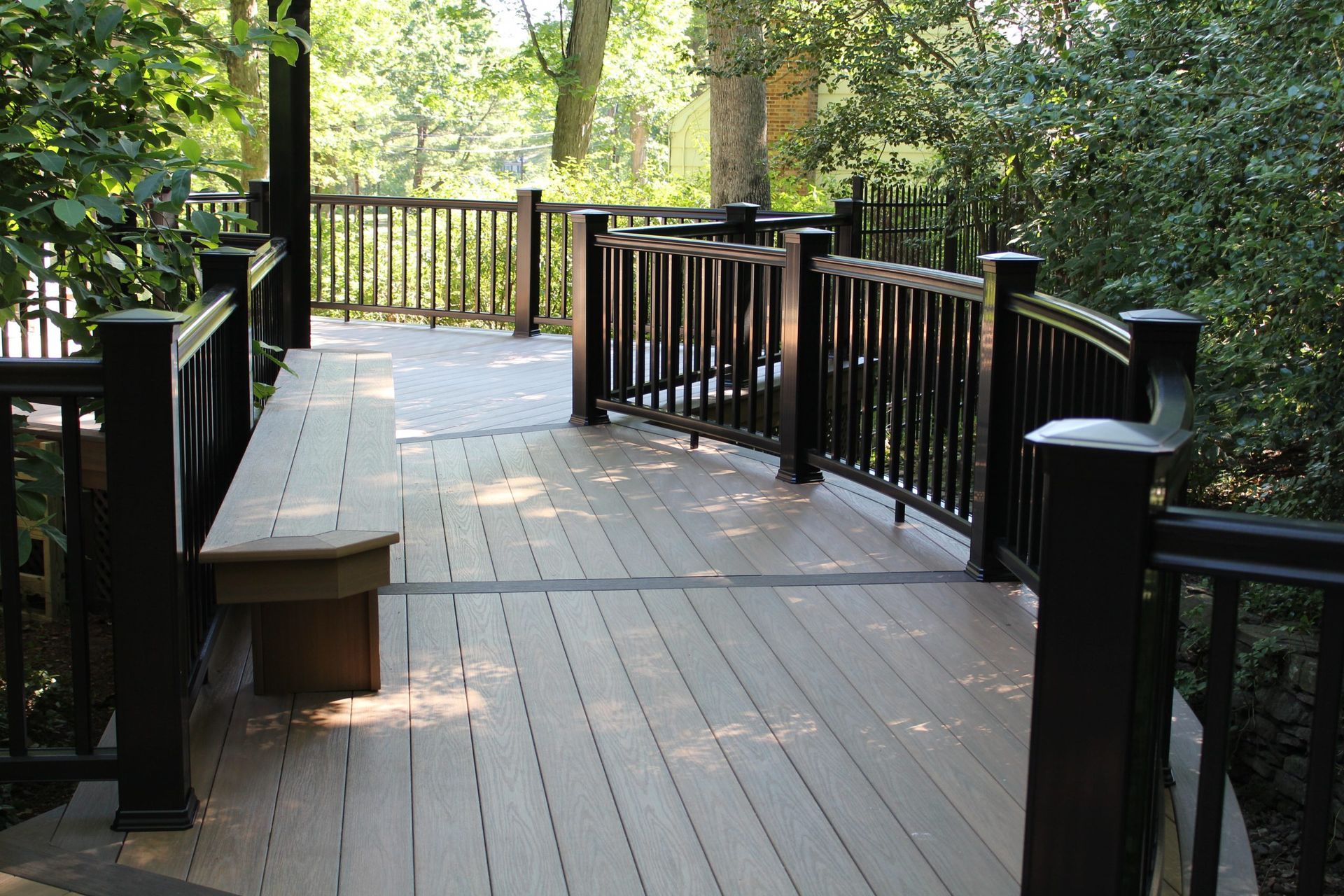 Curved composite deck with built-in bench and black railing by New Dimensions NJ