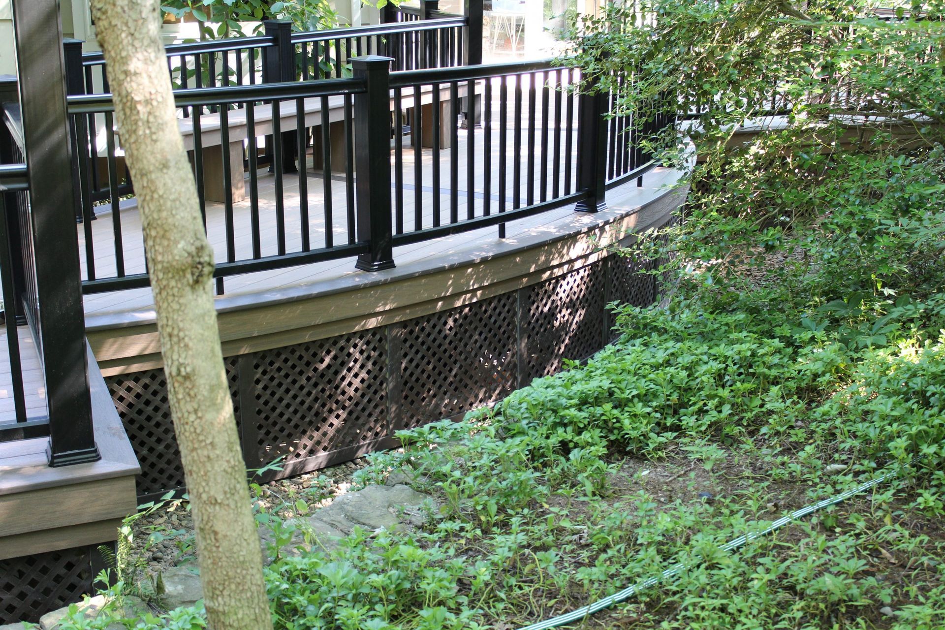 Curved deck with black railings surrounded by lush greenery built by New Dimensions Deck NJ