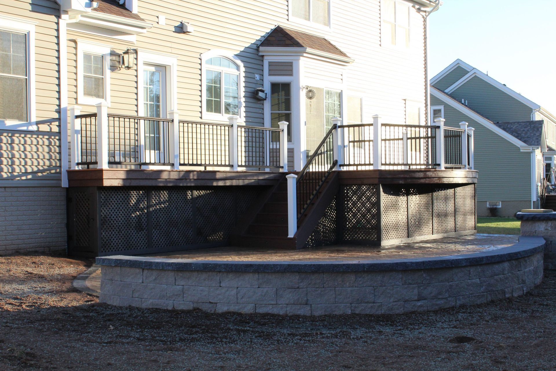 Composite deck with white and black railings over stone patio built by New Dimensions NJ