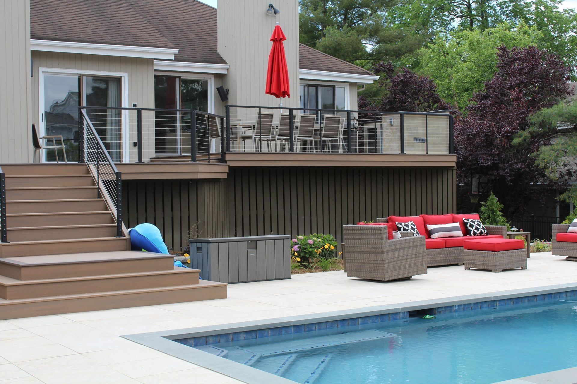 Modern poolside deck with cable railings and red cushioned furniture built by NJ deck builders