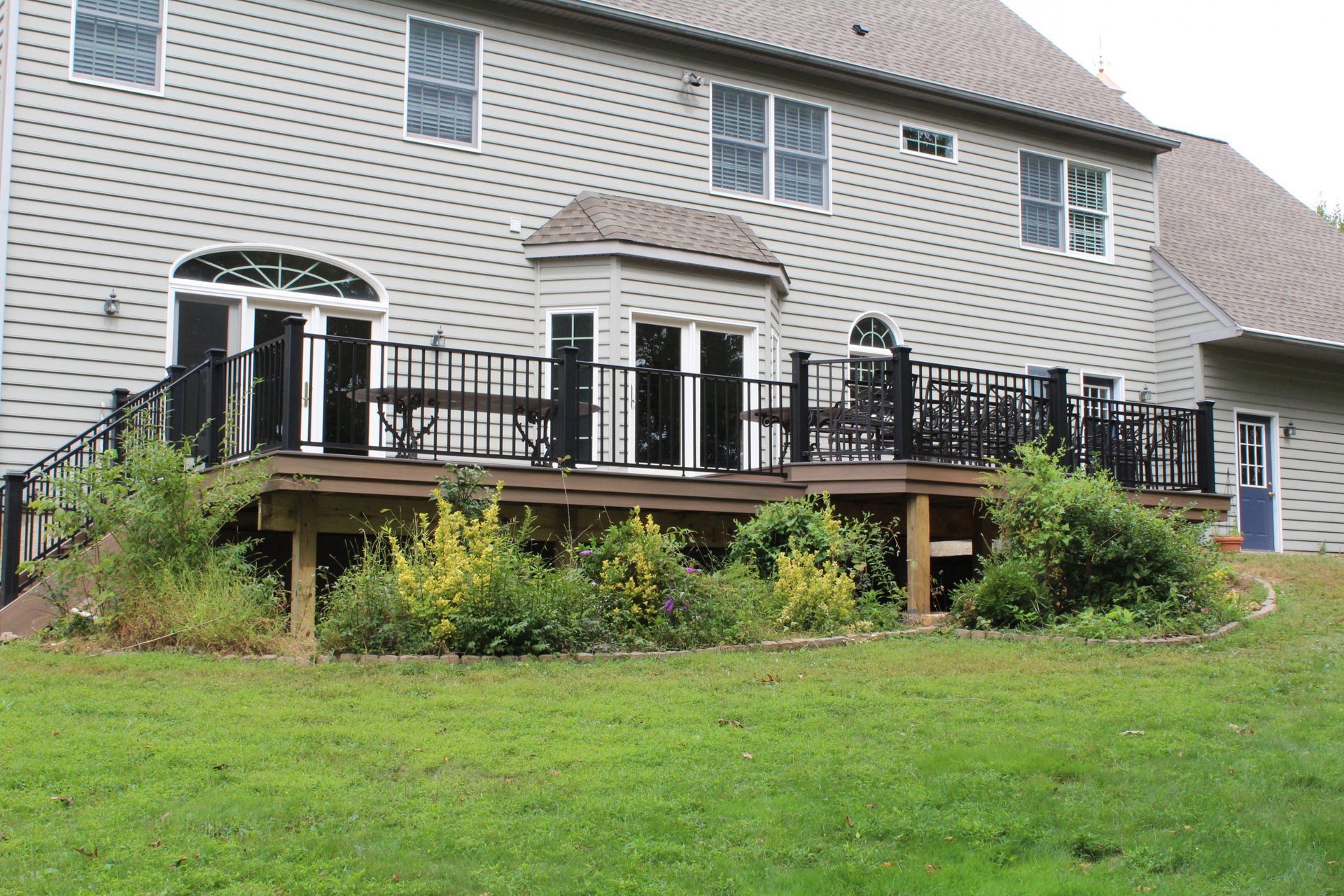 Backyard deck with black railings and surrounding greenery.