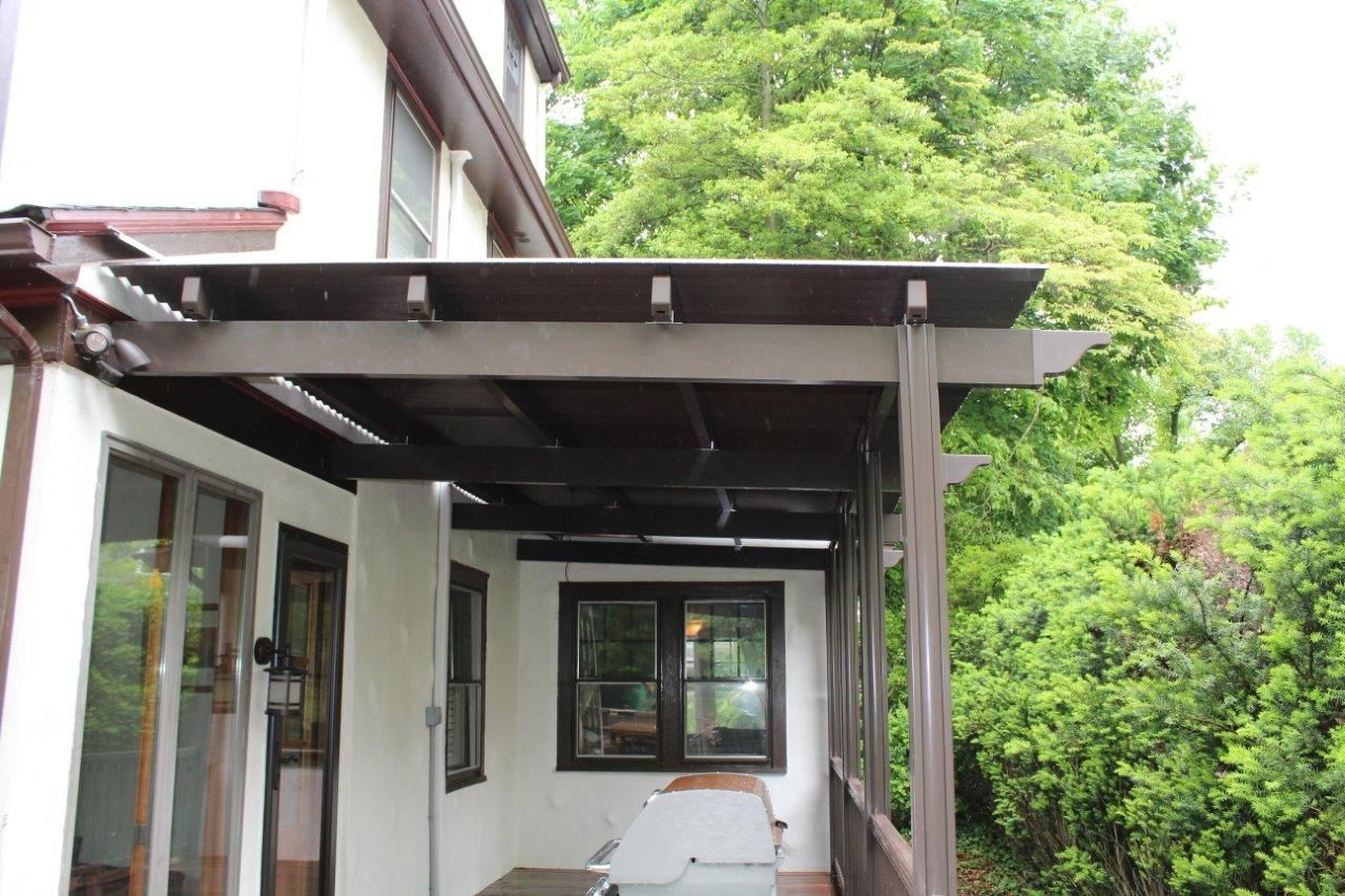 A porch with a pergola and a table in front of a house surrounded by trees.