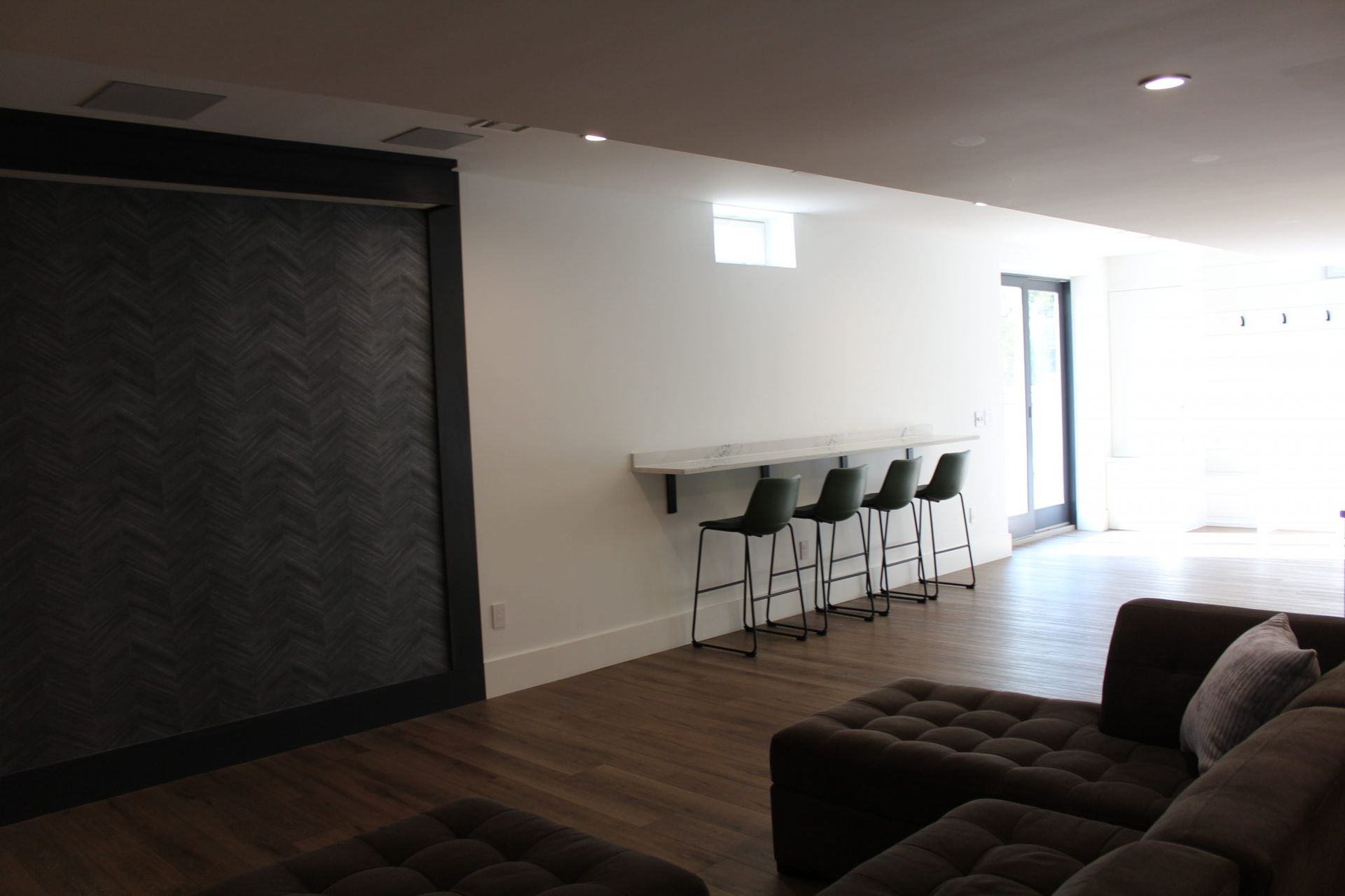Open basement with bar seating, wooden flooring, and natural light from glass doors.