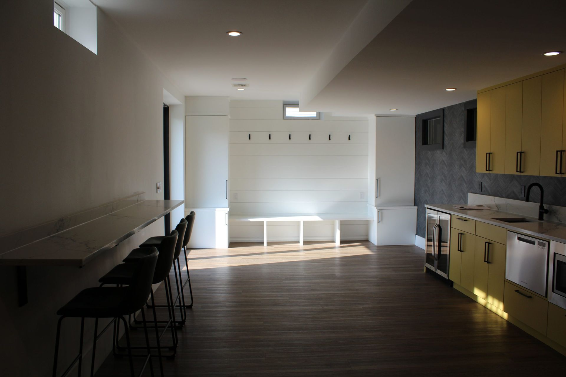 Empty, sunlit room with a bar, kitchen, and seating.