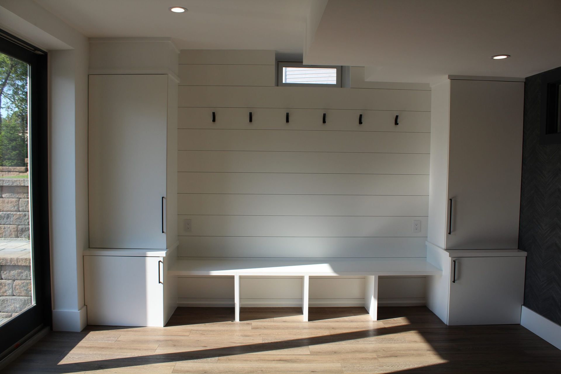 White entryway with built-in cabinets, bench, and hooks on a shiplap wall.