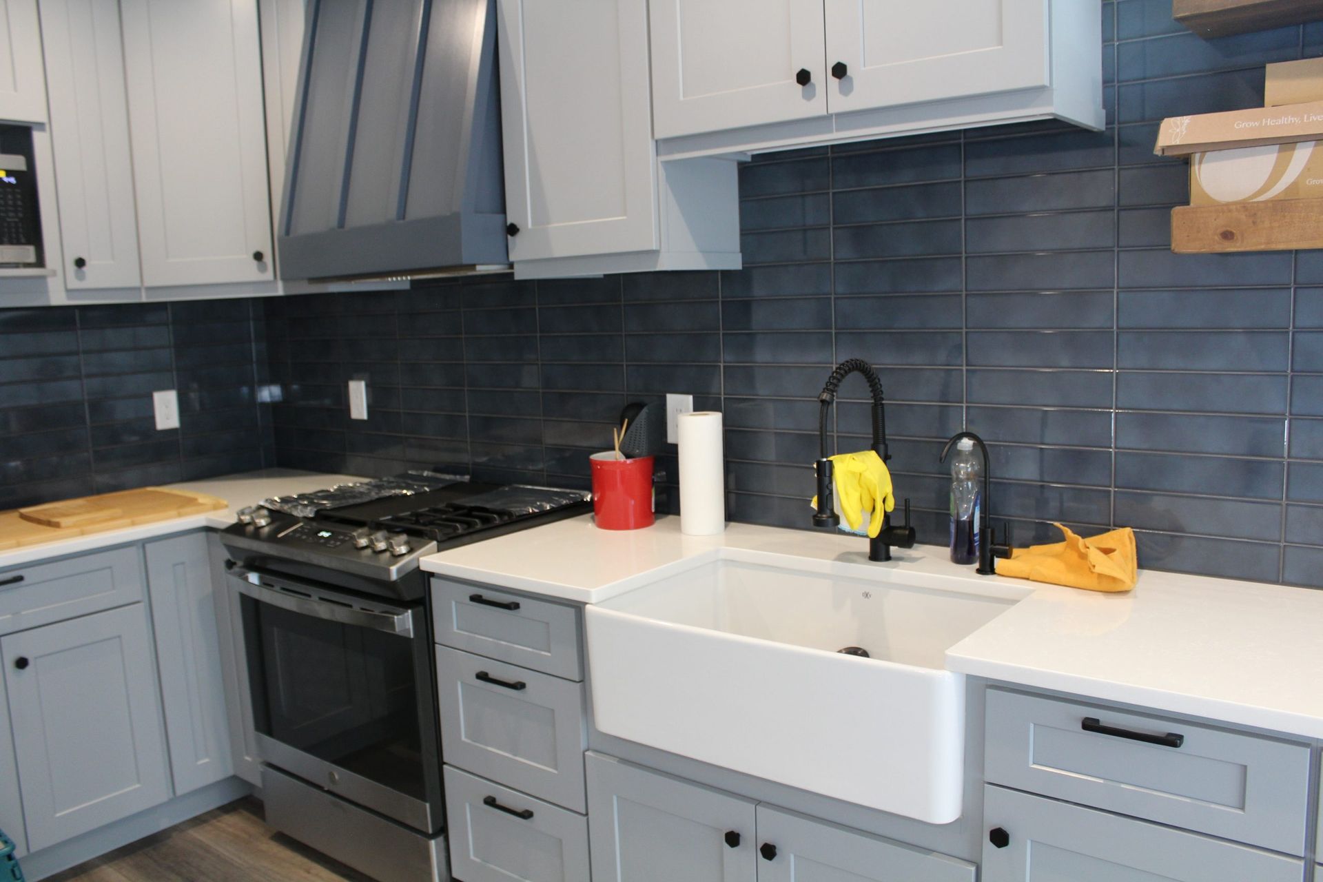 Kitchen with gray cabinets, white countertops, dark blue backsplash, and a white farmhouse sink.
