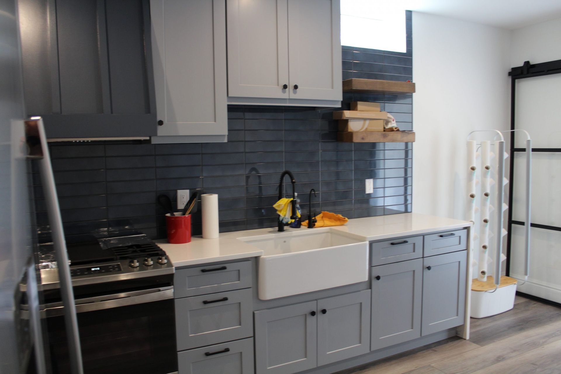 Gray and white kitchen with a farmhouse sink, stainless steel appliances, and a black subway tile backsplash.