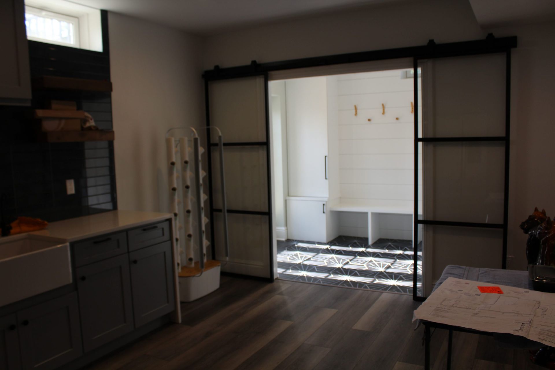 A doorway with sliding black framed glass doors leads to a white-walled mudroom.