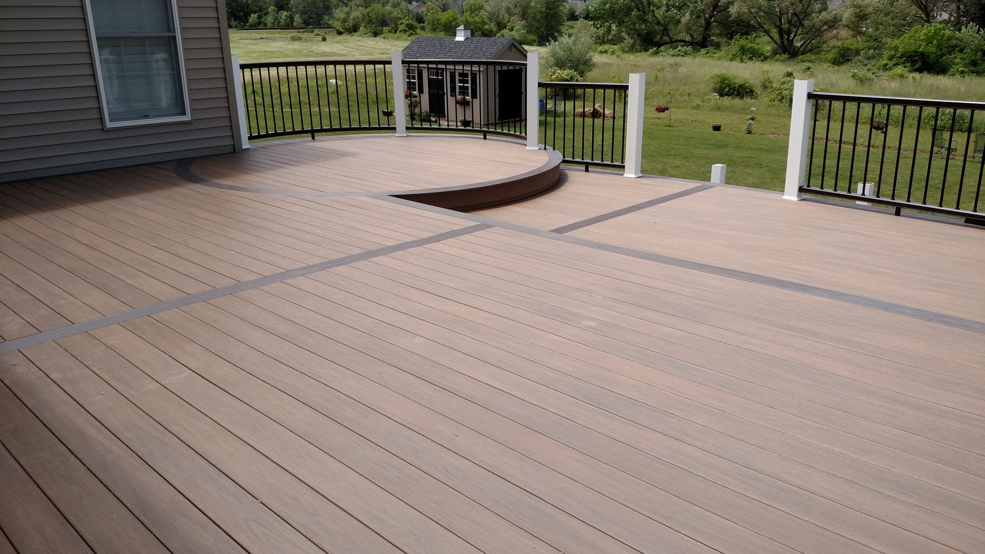 Modern composite deck with circular design and black-and-white railing overlooking yard.