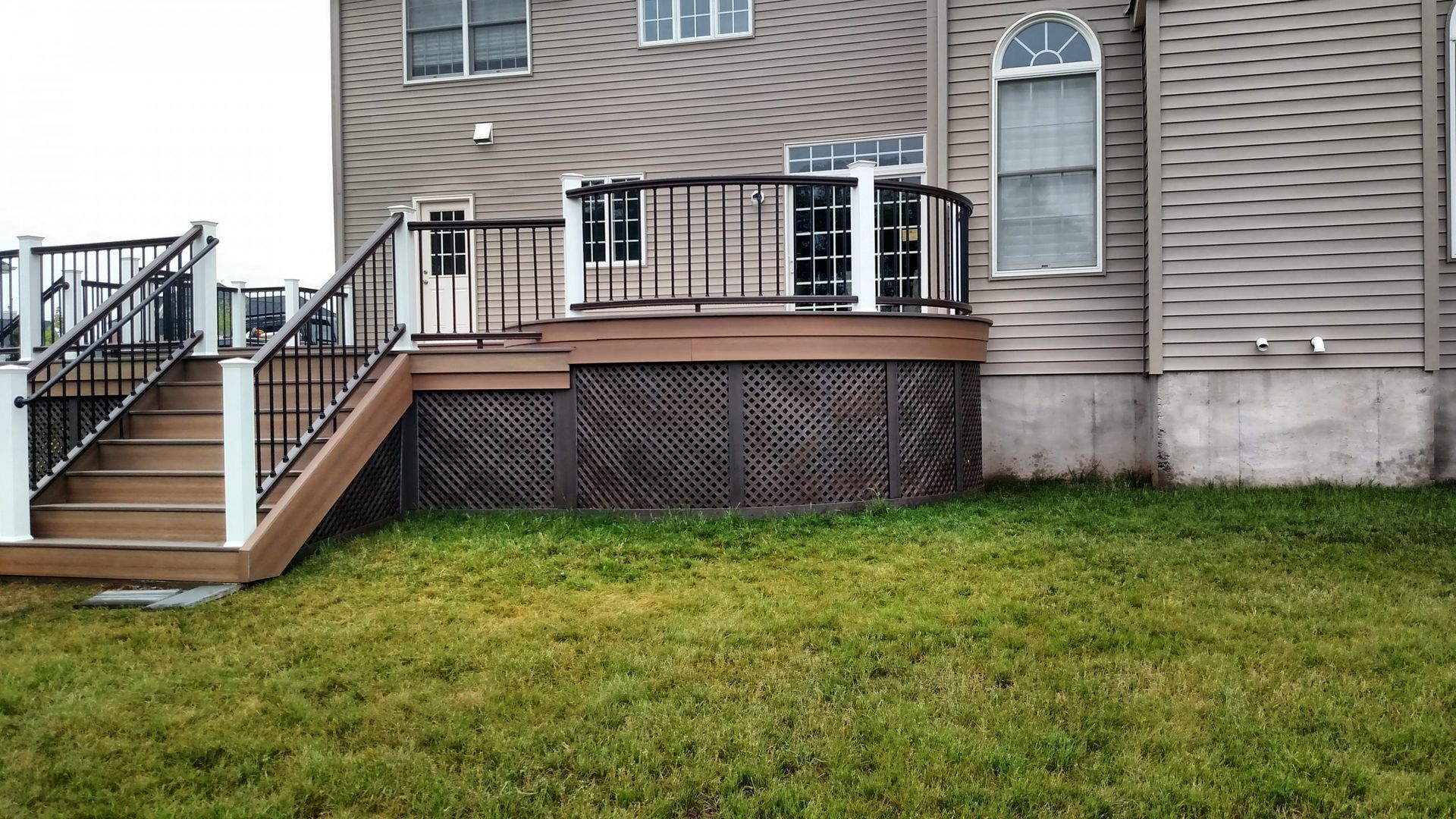 Raised brown deck with lattice skirting and white posts with black metal railings.