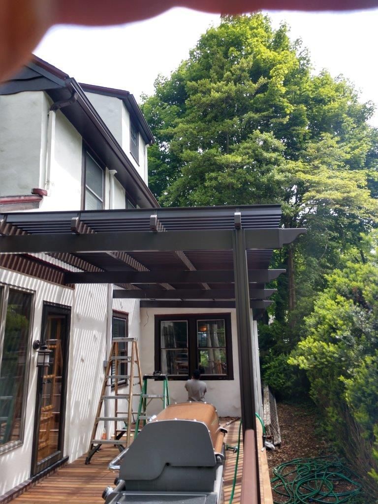 A motorcycle is parked under a pergola in front of a house.