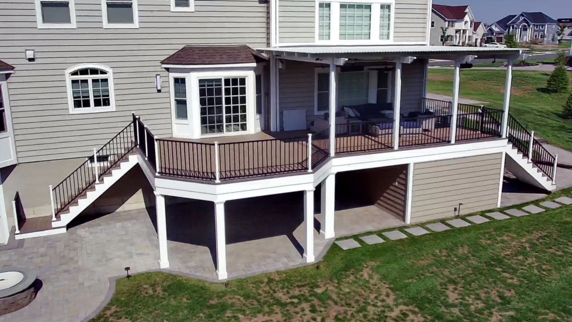 Rear view of two-story house with expansive deck, covered seating, and paved patio below.