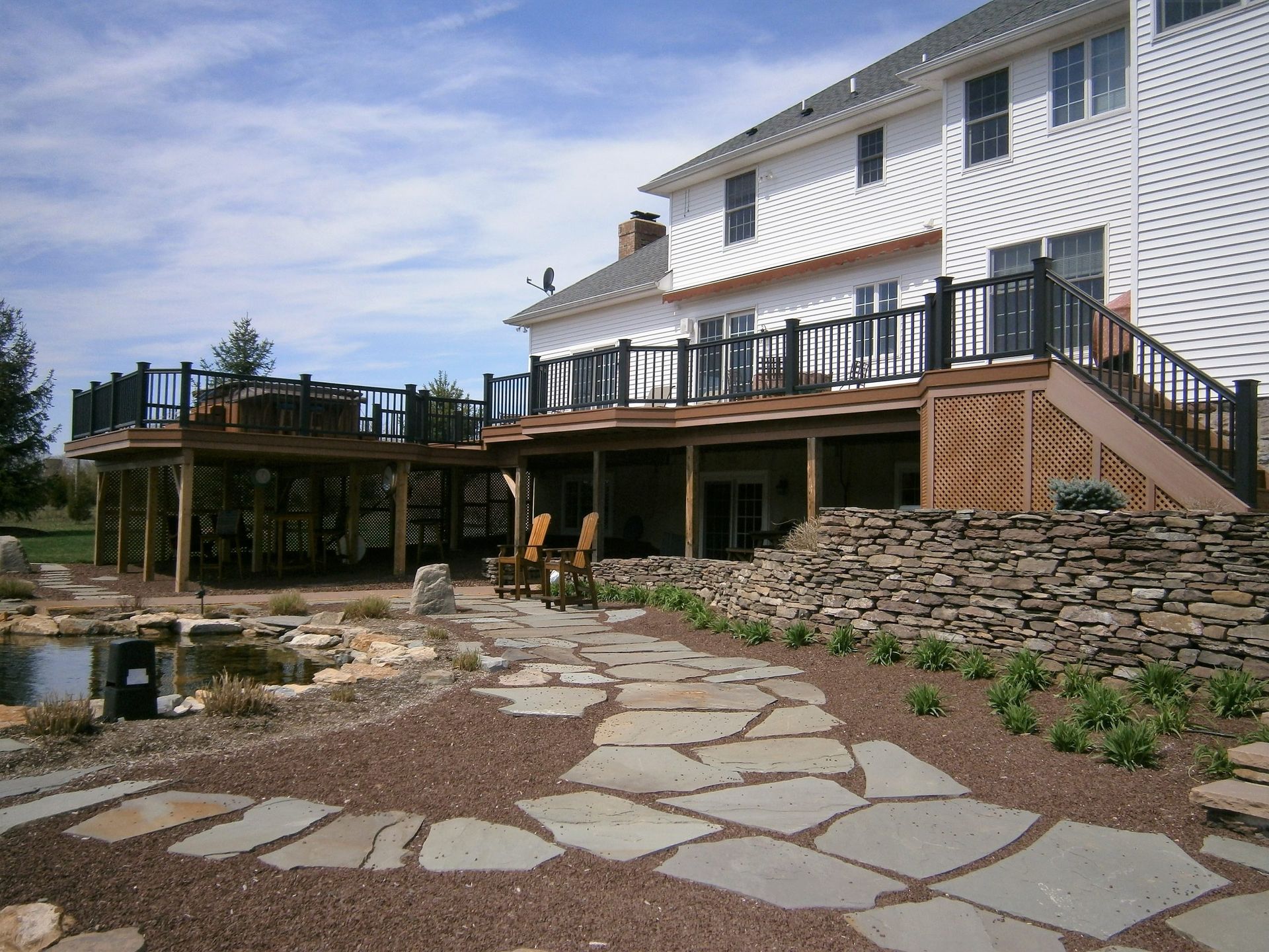 Multi-level deck with black railings and stone retaining walls beside landscaped pond.