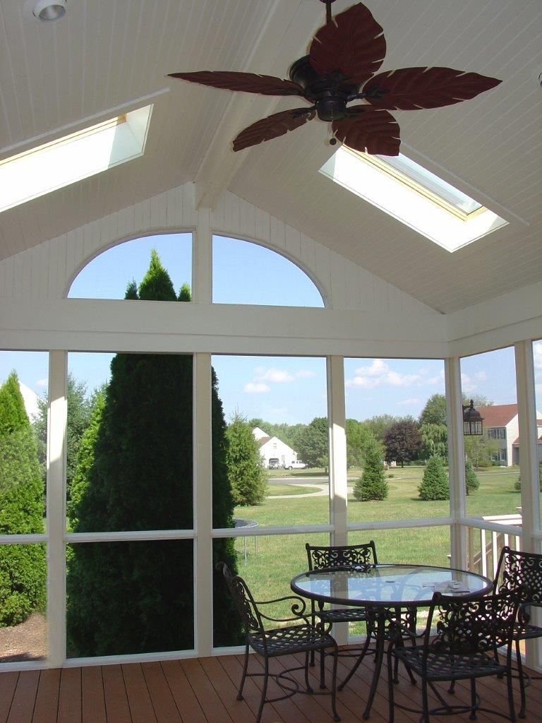 A screened in porch with a table and chairs and a ceiling fan