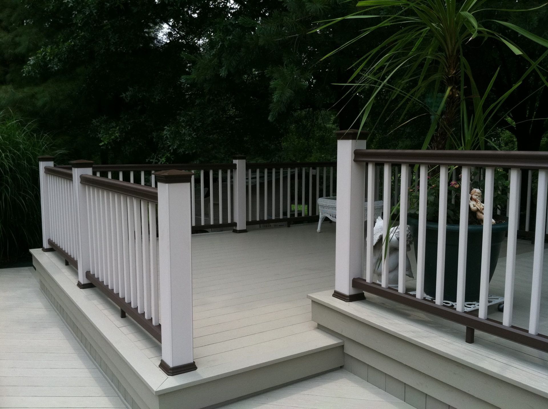 Gray composite deck with brown railings and potted plants under shaded trees.