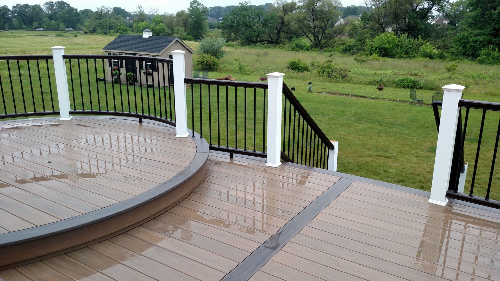 Curved deck section with white posts and black railings overlooking grassy backyard.